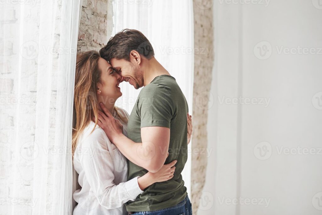 attractive youth lovely couple kissing and enjoying each other near the window of their new home photo
